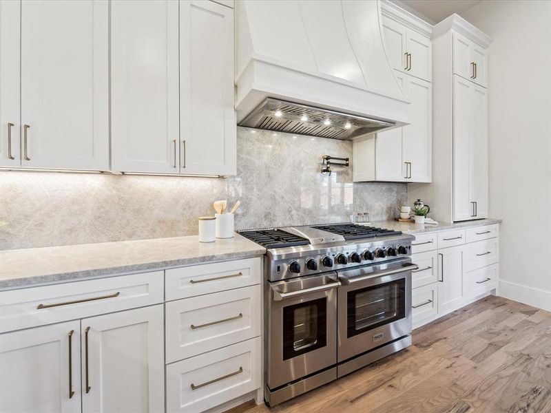 Kitchen with double oven range, premium range hood, white cabinets, decorative backsplash, and light hardwood / wood-style floors