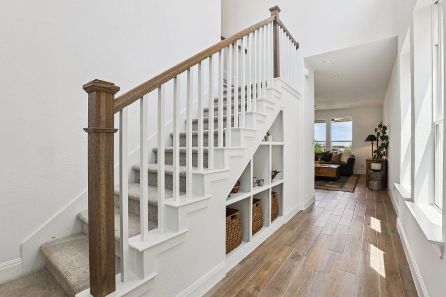 A welcoming entryway featuring a staircase with carpeted treads and a wooden handrail, built-in shelving under the stairs, and wood-look tile flooring
