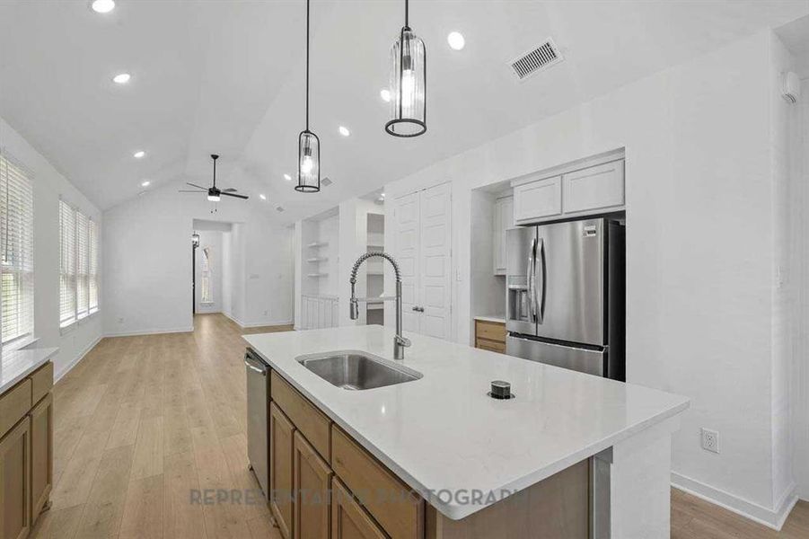 Kitchen with lofted ceiling, light wood-style floors, stainless steel appliances, pendant lighting, and a kitchen island with sink