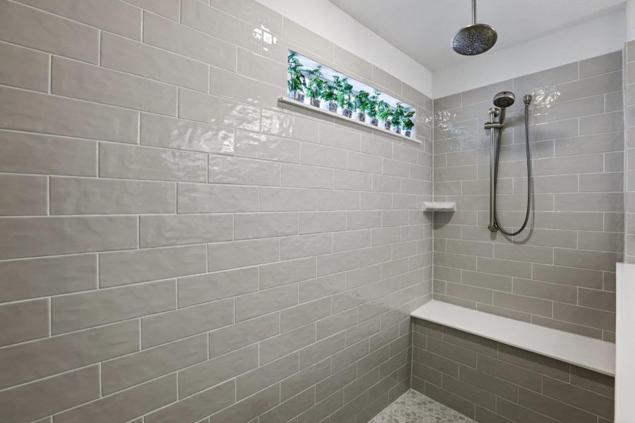 Shower featuring light grey subway tiles, a built-in bench, and a rain shower head with an additional handheld shower