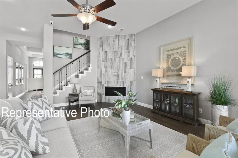 Living area featuring dark wood-finish flooring, a contemporary ceiling fan, and a fireplace with a light-toned wood panel surround Living area featuring dark wood-finish flooring, a contemporary ceiling fan, and a fireplace with a light-toned wood panel surround