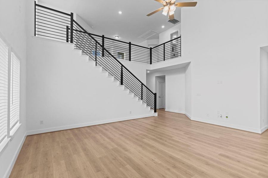 A wide-angle view of the family room highlights the striking iron staircase, soaring ceilings, and expansive wood like tile flooring that flows beautifully throughout the main living areas—creating a grand yet.  Down private hallway you will discover the Primary suite tucked away for privacy! **Image Representative of Plan Only and May Vary as Built**.  WHAT A WOW FACTOR