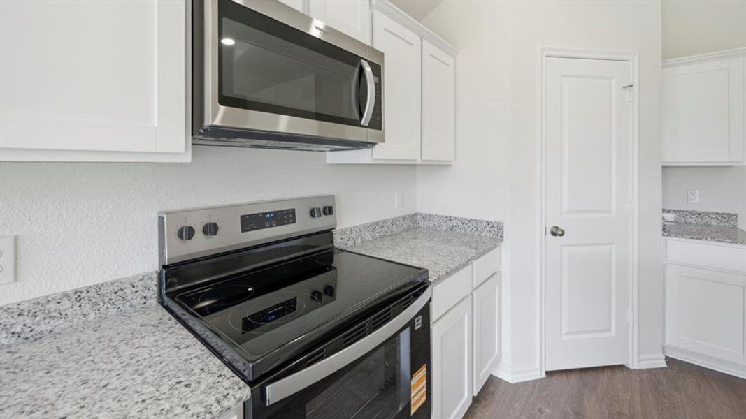 Kitchen featuring stainless steel appliances, light stone countertops, white cabinetry, and dark wood finished floors
