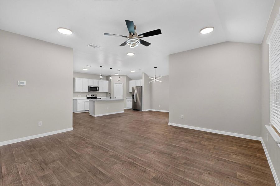 Rich wood-inspired flooring anchors a spacious open layout leading into the kitchen.