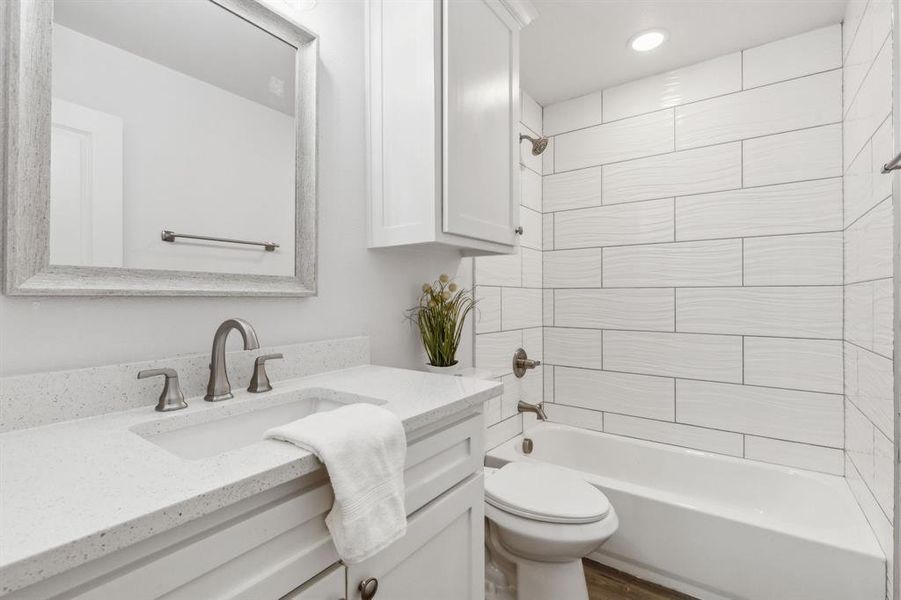 Full bathroom featuring vanity, wood-type flooring, tiled shower / bath, and toilet