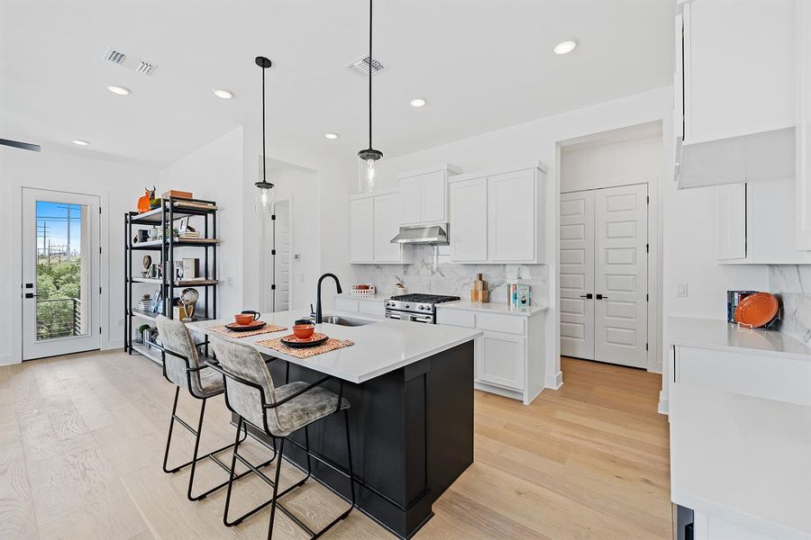 Kitchen with stainless appliances, gas range and fan, center island with sink, pendant lights and surrounding recessed lighting Kent Moore cabinetry, wood flooring