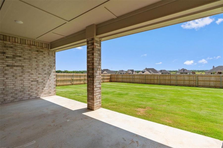 Covered patio featuring a brick wall, concrete flooring, and recessed lighting, opening to a spacious lawn with a wood privacy fence Covered patio featuring a brick wall, concrete flooring, and recessed lighting, opening to a spacious lawn with a wood privacy fence