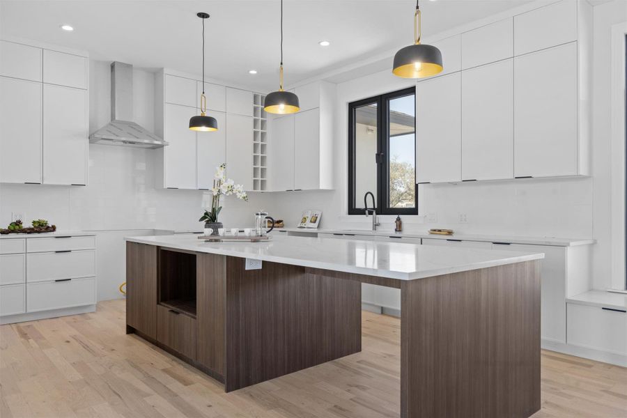 Kitchen featuring light wood finished floors, a center island, wall chimney range hood, white cabinets, and modern cabinets