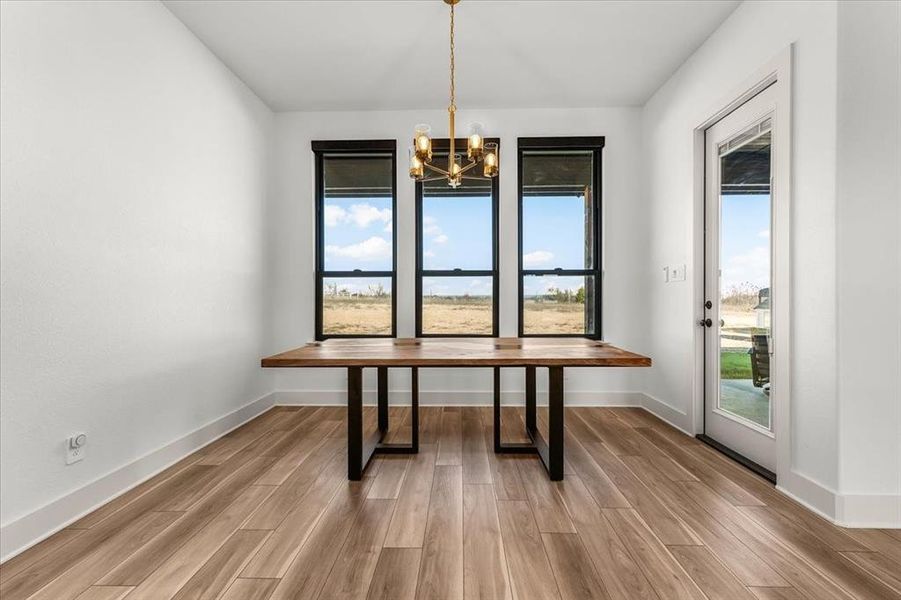 Large dining space with modern triple black framed windows & tasteful gold chandelier complementing luxury vinyl plank color tones.  Back door leads to back patio.