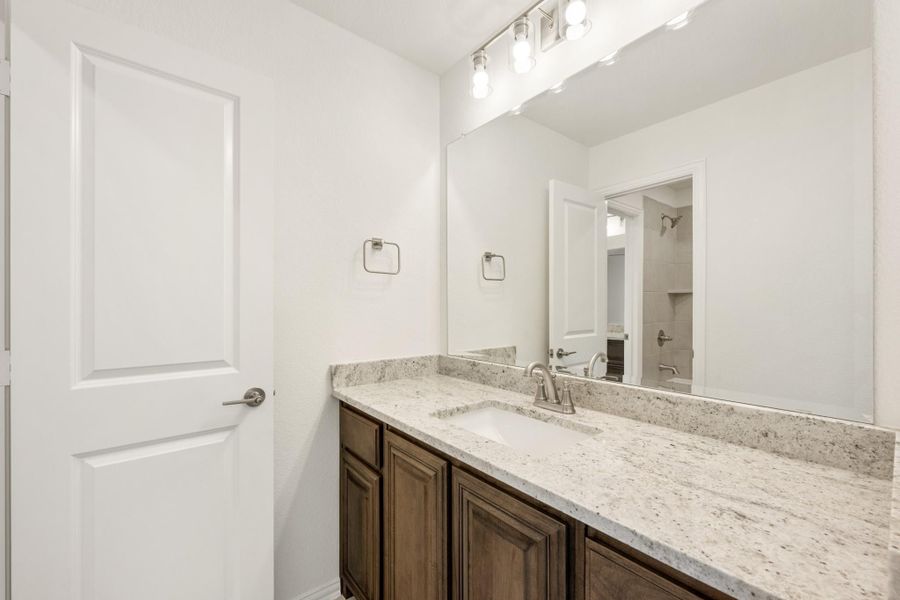 Bathroom vanity with dark wood cabinets, granite countertop, single sink, and large mirror with overhead lighting. Bathroom vanity with dark wood cabinets, granite countertop, single sink, and large mirror with overhead lighting.