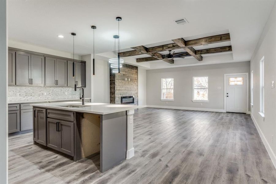 Kitchen with a center island with sink, ceiling fan, decorative backsplash, beamed ceiling, and light hardwood / wood-style floors