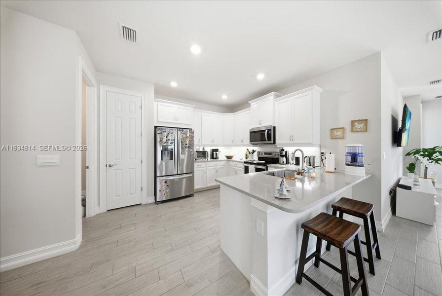 featuring appliances with stainless steel finishes, a kitchen bar, white cabinets