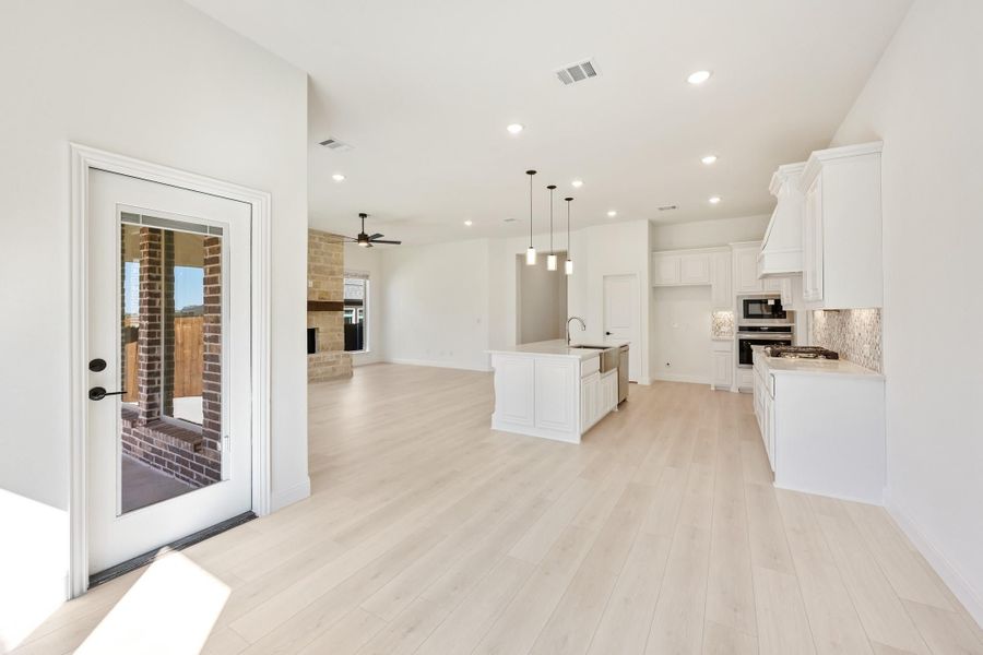 Open-concept kitchen and living area with white cabinets, center island, light wood floors, and back door access. Open-concept kitchen and living area with white cabinets, center island, light wood floors, and back door access.