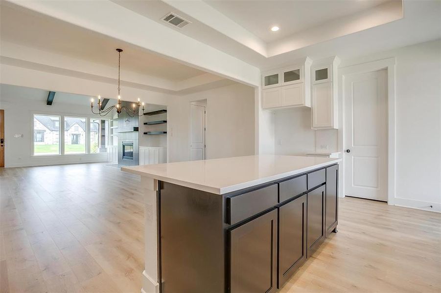 Kitchen with light wood-type flooring, a chandelier, a center island, a tray ceiling, and white cabinets