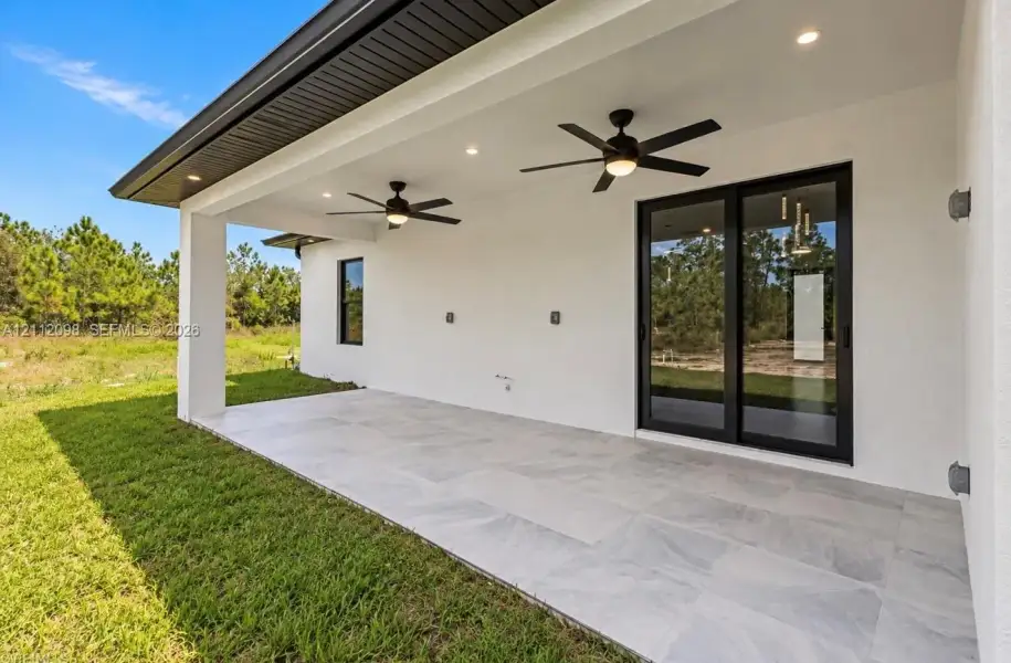 Covered patio featuring large-format tile flooring, dual ceiling fans, recessed lighting, and black-framed sliding glass doors Covered patio featuring large-format tile flooring, dual ceiling fans, recessed lighting, and black-framed sliding glass doors