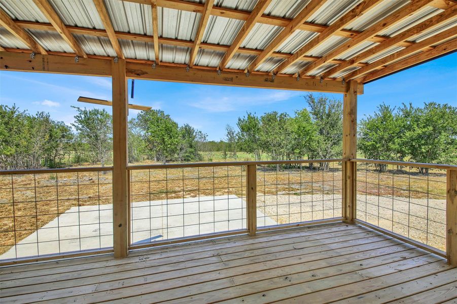 A spacious covered wood deck looks out over expansive green fields and mature trees.