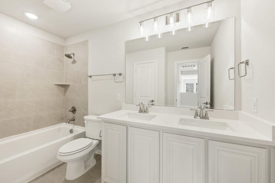 Bathroom with double sink vanity, white cabinets, tub-shower combo, and large mirror with overhead lighting