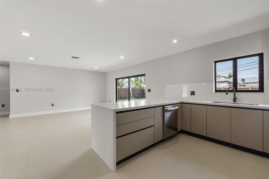 Kitchen featuring flat-panel cabinetry, light-toned stone-finish countertops, recessed ceiling lighting, large-format tile flooring, and matte black plumbing fixtures