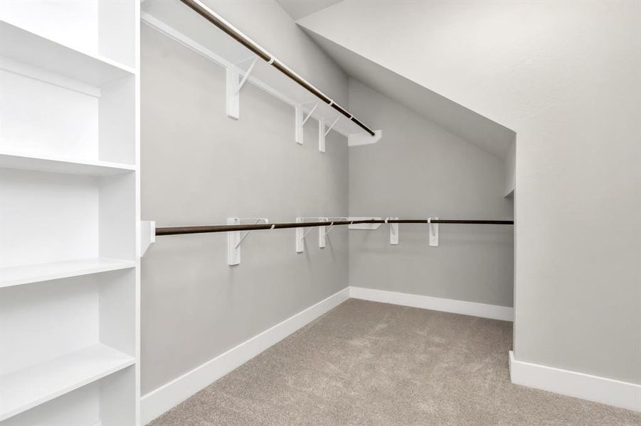 Explore the roomy walk-in closet adorned with shelving, plush carpet, custom paint, and dark modern finishes. Sample photo of completed home with similar floor plan. As-built interior colors and selections may vary.