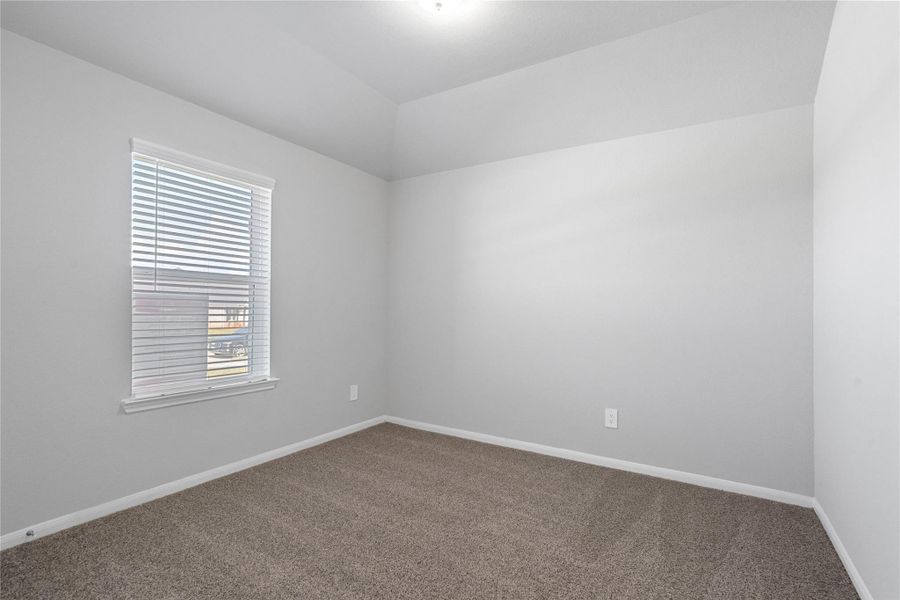 Tucked peacefully in the front of this home is a secondary bedroom perfect for guests or a quiet home office. It features soft plush carpeting, a window with fitted blinds, sloped ceiling, and ample sized closet space.