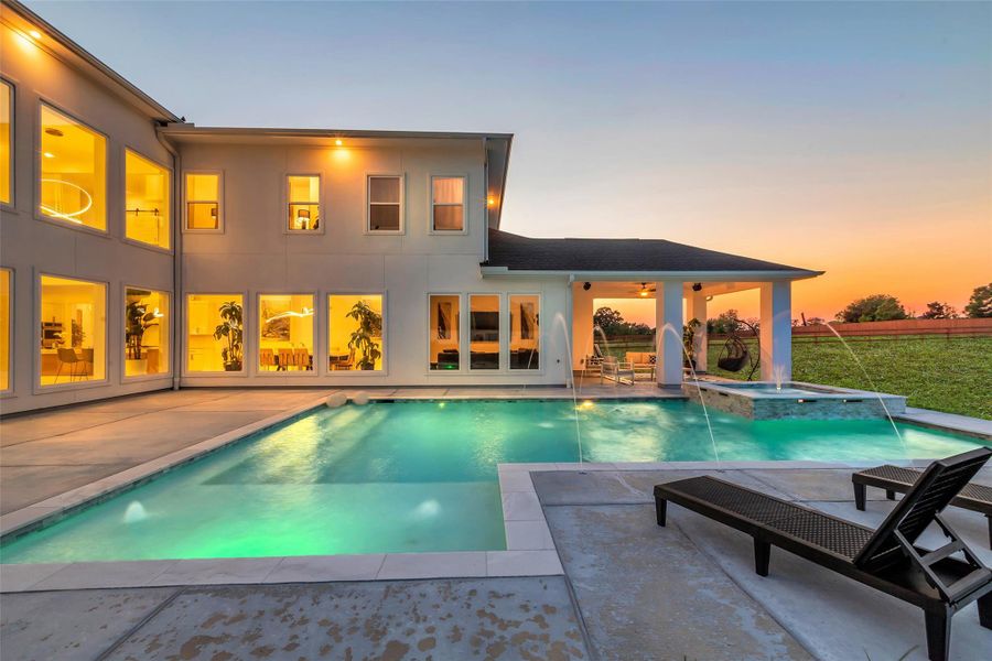 Twilight Luxury Retreat: As the sun sets, the pool and spa come alive with glowing water features and illuminated fountains. The covered patio creates a seamless indoor-outdoor connection, while expansive windows frame the backyard from nearly every angle of the home. A resort-caliber setting designed for both relaxation and refined entertaining.
