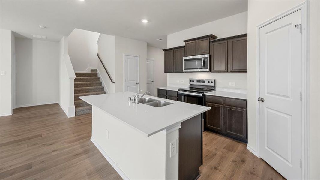 Kitchen featuring stainless steel appliances, a center island with sink, dark wood finish cabinetry, dark wood finished floors, and recessed lighting