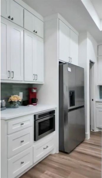 Contemporary kitchen featuring white shaker cabinetry, stainless steel refrigerator, built-in microwave, white countertops, and wood-finish flooring