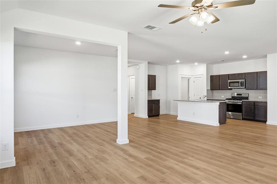 Kitchen featuring stainless steel appliances, dark wood finish cabinetry, a ceiling fan, an island with sink, and recessed lighting
