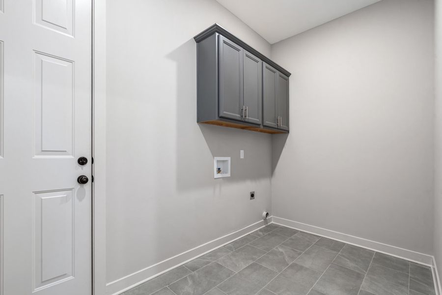 Grey shaker-style cabinetry with wood-finish trim, tile flooring, and white paneled door