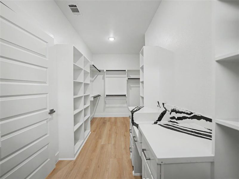 Custom closet system with extensive shelving, multiple hanging rods, built-in drawers, wood-finish flooring, and a modern paneled door Custom closet system with extensive shelving, multiple hanging rods, built-in drawers, wood-finish flooring, and a modern paneled door