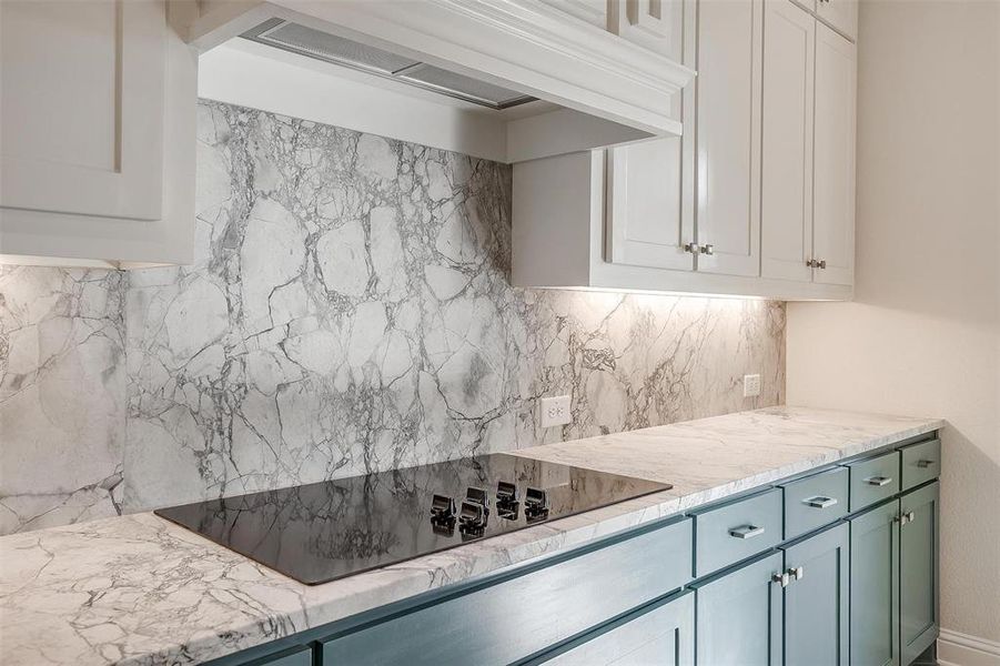 Kitchen featuring white cabinetry, light stone countertops, tasteful backsplash, black electric cooktop, and custom range hood