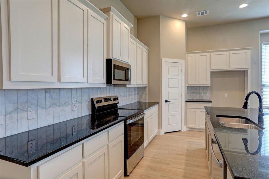 Kitchen with stainless steel appliances, backsplash, dark stone countertops, white cabinets, and recessed lighting Kitchen with stainless steel appliances, backsplash, dark stone countertops, white cabinets, and recessed lighting