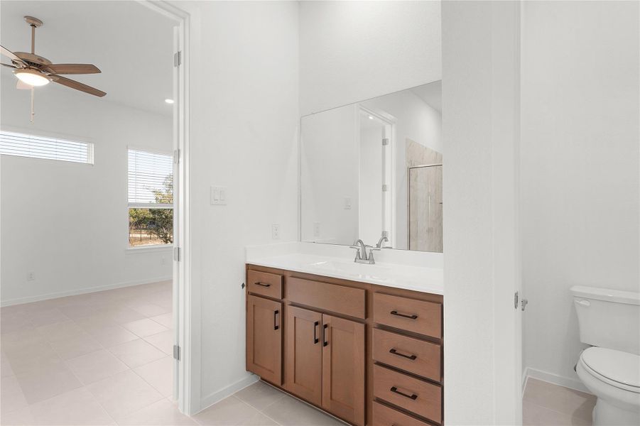 Bathroom with toilet, a ceiling fan, vanity, a shower stall, and baseboards