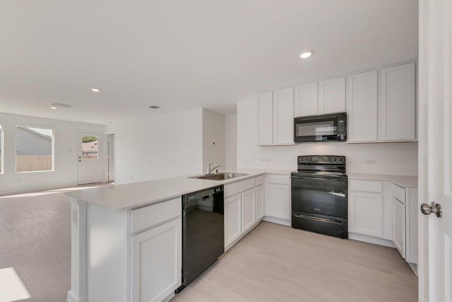 Kitchen featuring black appliances, light countertops, white cabinets, recessed lighting, and open floor plan