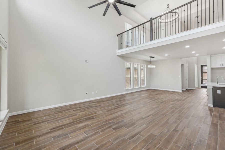 Unfurnished living room with a towering ceiling, ceiling fan, wood finished floors, baseboards, and a chandelier Unfurnished living room with a towering ceiling, ceiling fan, wood finished floors, baseboards, and a chandelier