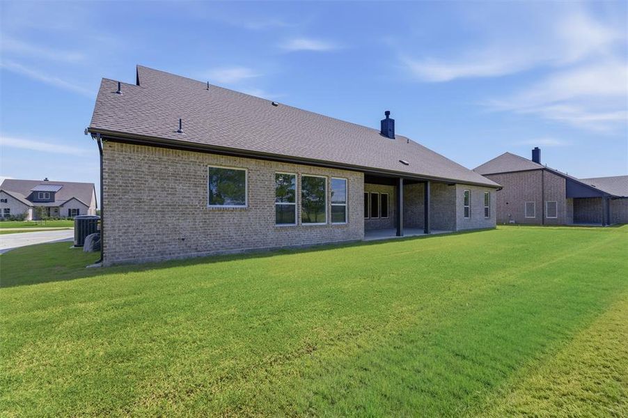 Expansive green lawn with a covered patio, brick exterior, and multiple windows Expansive green lawn with a covered patio, brick exterior, and multiple windows