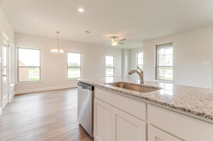 Kitchen with sink, dishwasher, white cabinetry, hanging light fixtures, and light stone counters