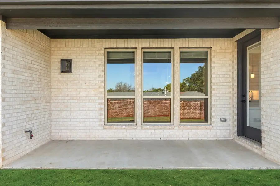 Covered back patio with concrete floor, light brick exterior, triple windows, and dark entry door