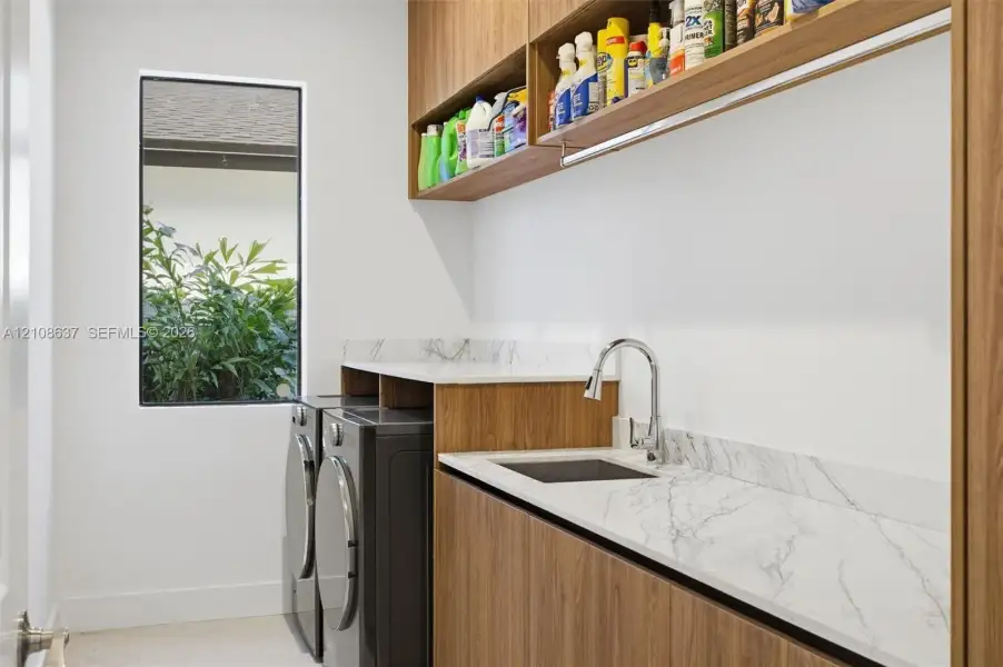 Laundry area featuring wood-finish cabinetry, stone-surface countertops, a drop-in sink with a gooseneck faucet, and open upper shelving