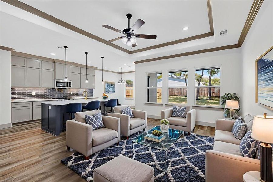 Living room featuring a raised ceiling, light wood-style floors, crown molding, ceiling fan, and recessed lighting