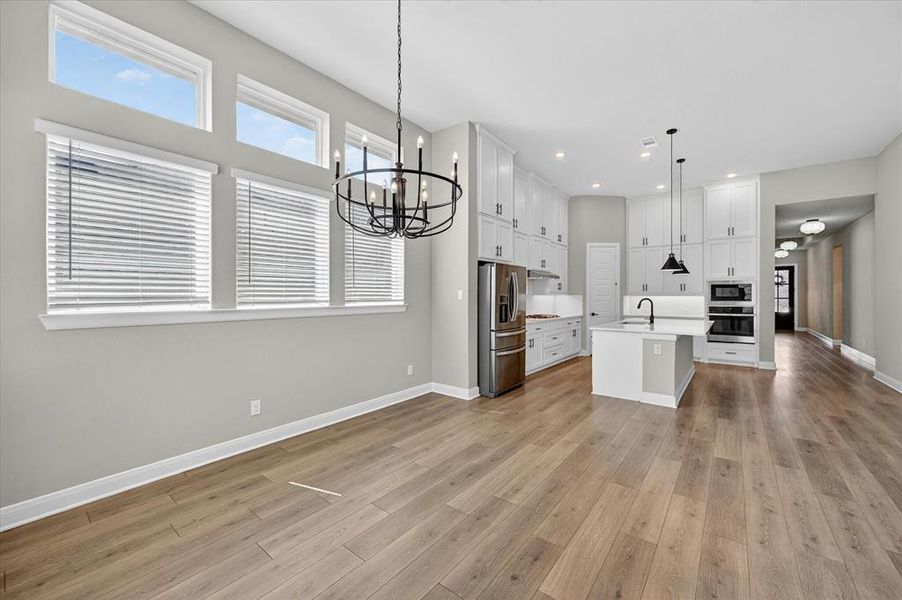 Open-concept interior featuring light wood-finish flooring, a contemporary black chandelier, and multiple windows Open-concept interior featuring light wood-finish flooring, a contemporary black chandelier, and multiple windows