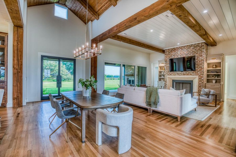 Dining room with a brick fireplace, a wood ceiling with exposed beams, hardwood / wood-style floors, a chandelier, and a high ceiling Dining room with a brick fireplace, a wood ceiling with exposed beams, hardwood / wood-style floors, a chandelier, and a high ceiling