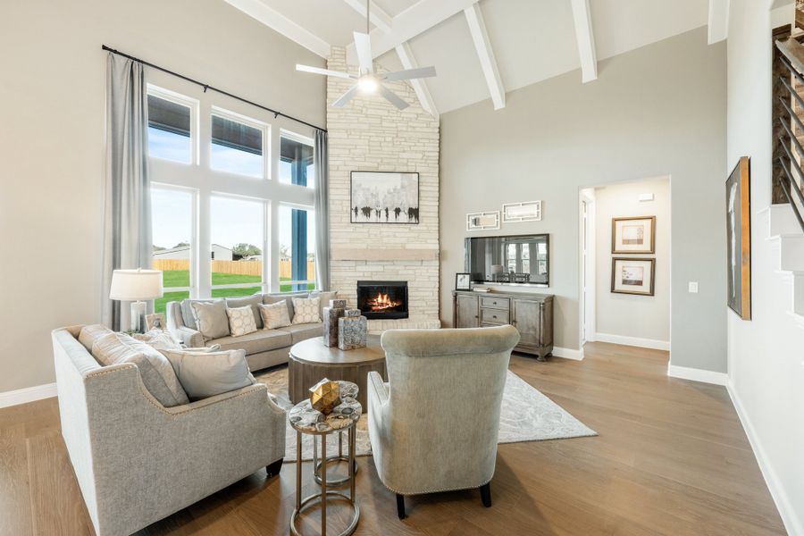 Living room with vaulted beamed ceiling, stone fireplace, hardwood floors, and large windows Living room with vaulted beamed ceiling, stone fireplace, hardwood floors, and large windows