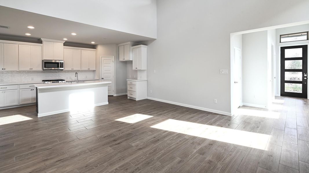 Kitchen featuring backsplash, white cabinetry, stainless steel microwave, dark wood finished floors, and a towering ceiling Kitchen featuring backsplash, white cabinetry, stainless steel microwave, dark wood finished floors, and a towering ceiling