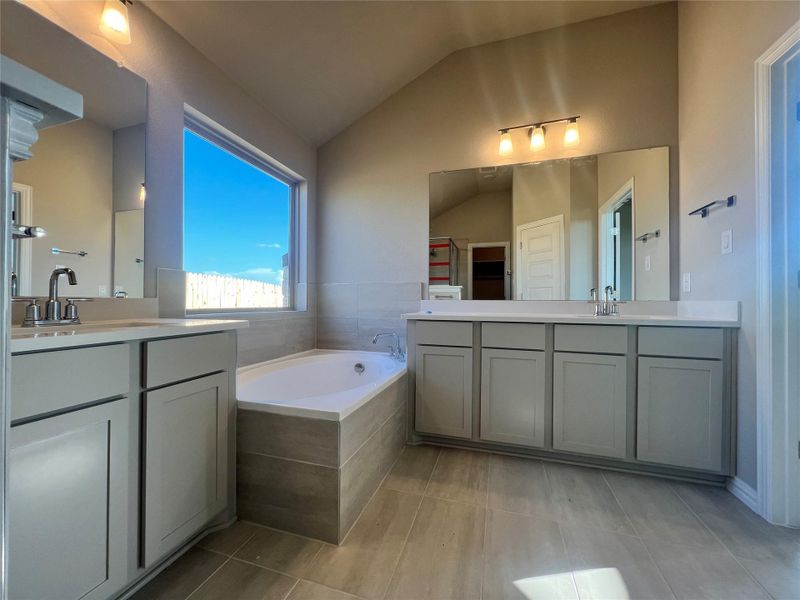 Bathroom with vaulted ceiling, a garden tub, two vanities, a spacious closet, and light tile patterned floors