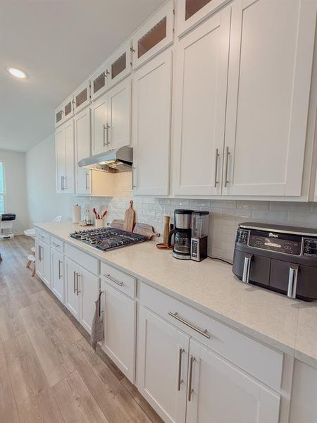 Kitchen featuring under cabinet range hood, stainless steel gas cooktop, light wood-style floors, white cabinets, and backsplash