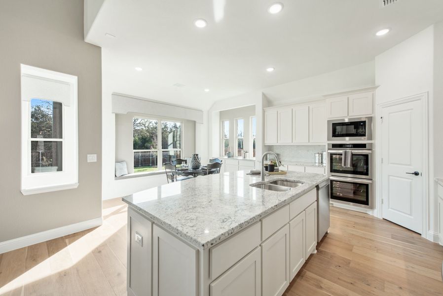 Kitchen with large granite island, white cabinets, stainless steel appliances, and hardwood floors open to living area Kitchen with large granite island, white cabinets, stainless steel appliances, and hardwood floors open to living area