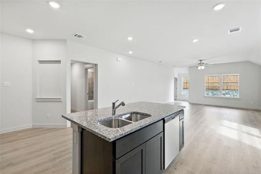 Kitchen featuring stainless steel dishwasher, a ceiling fan, light wood-style flooring, a center island with sink, and light stone countertops