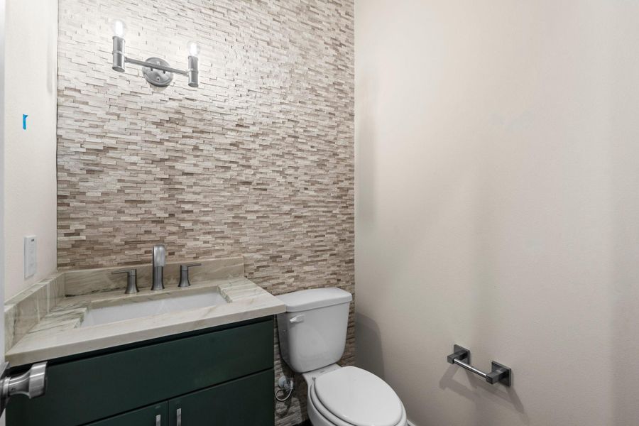 Stylish powder room with a limestone accent wall, modern lighting, and sleek vanity