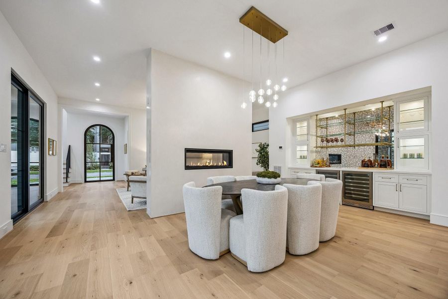 This room is a sophisticated modern dining space with a warm, upscale ambiance and clean architectural lines. The focal point of the room is a 14 Light Modern Bubble Crystal, Gold Raindrop Rectangle Chandelier.
